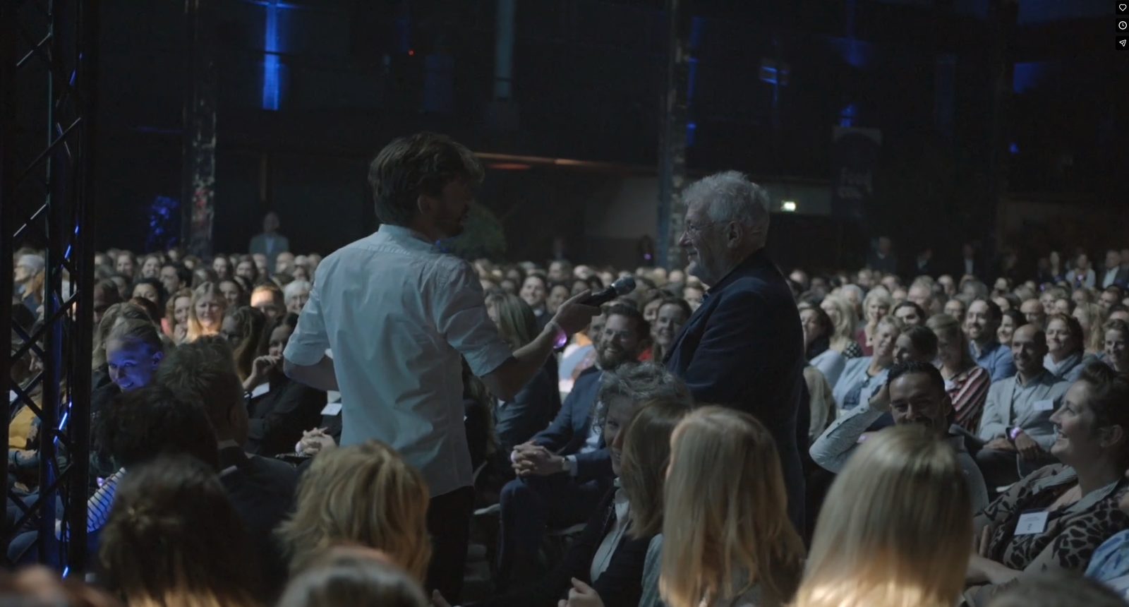 Steye van Dam als dagvoorzitter met microfoon bij een deelnemer in een volle zaal